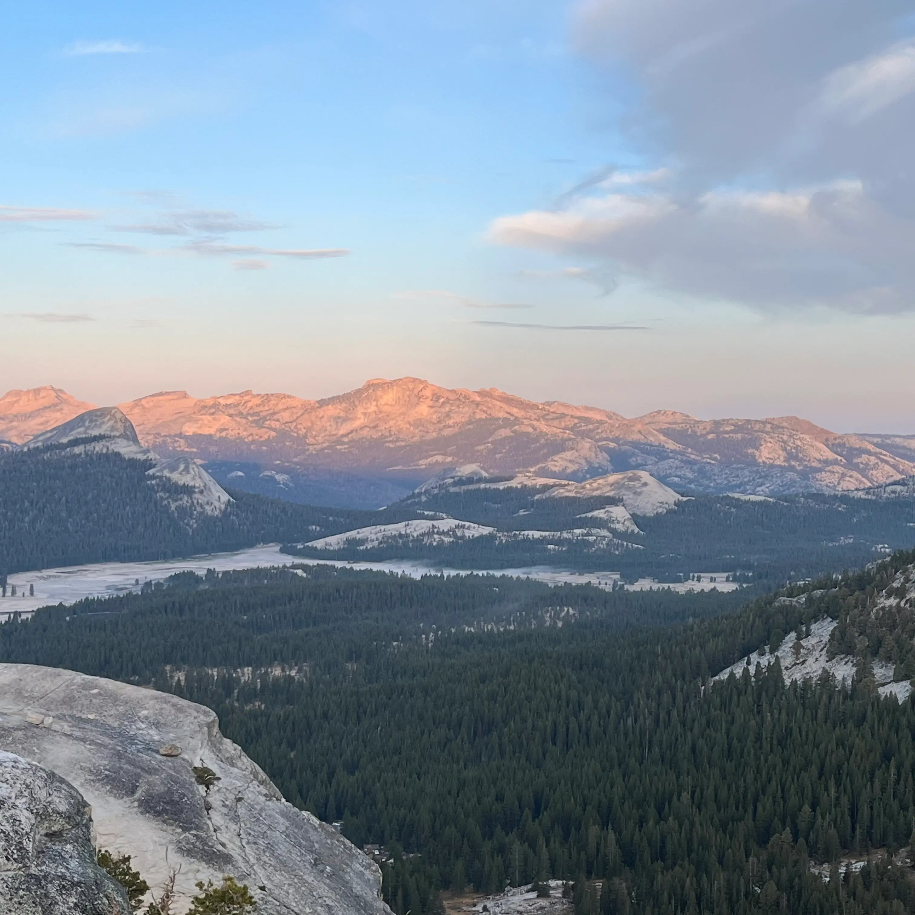 Sunrise alpenglow over granite mountains and forested valley